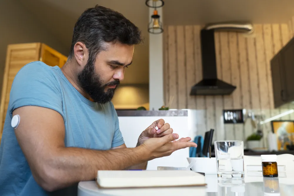 Hombre con un sensor de glucosa en el brazo revisando su glucosa en la cocina de su casa
