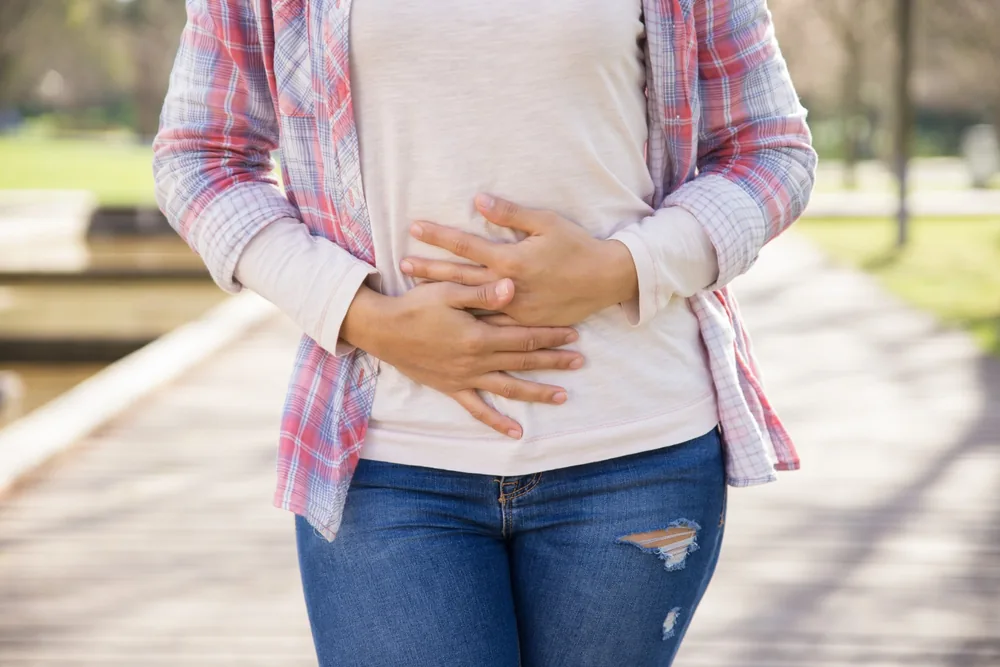Mujer con las manos sobre el abdomen por una molestia mientras camina por un parque