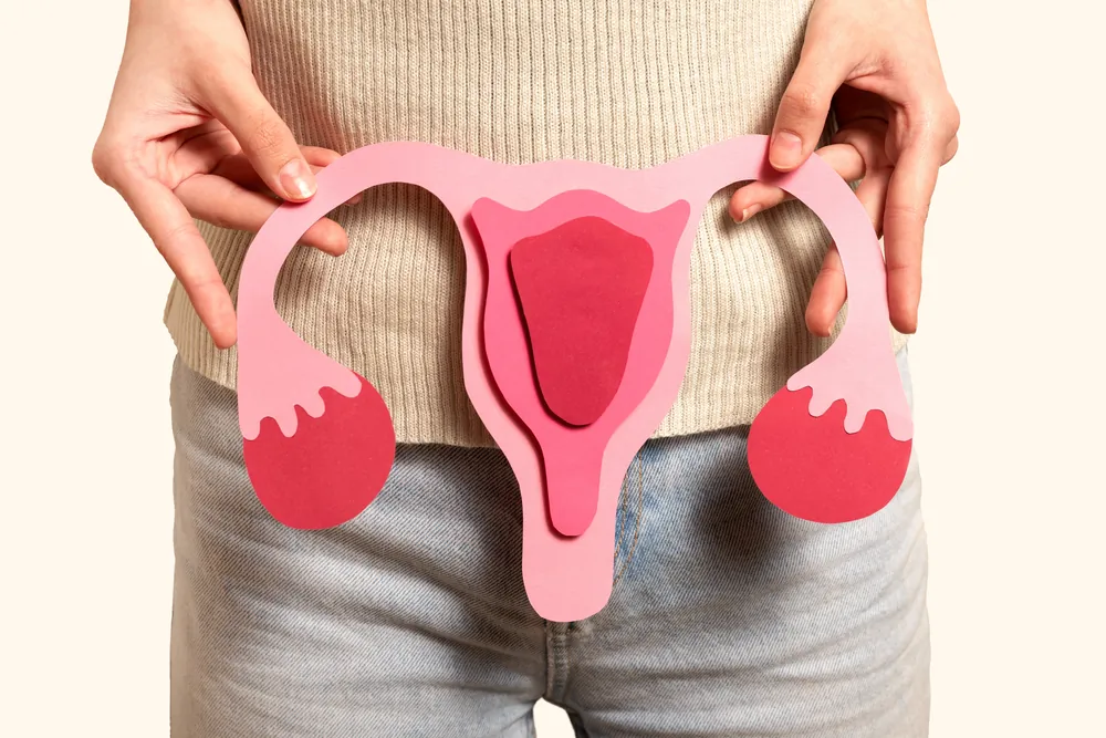 Mujer sosteniendo una figura de papel del útero y los ovarios frente a su abdomen