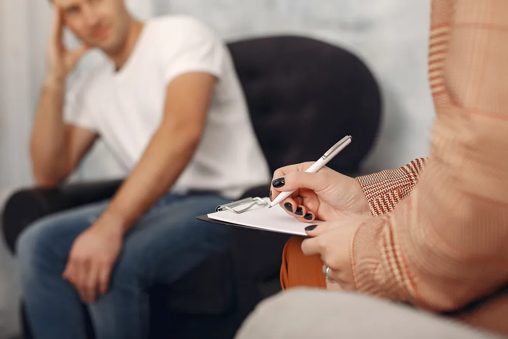 Paciente con la mano en la frente conversando con su psicóloga en una sesión de terapia
