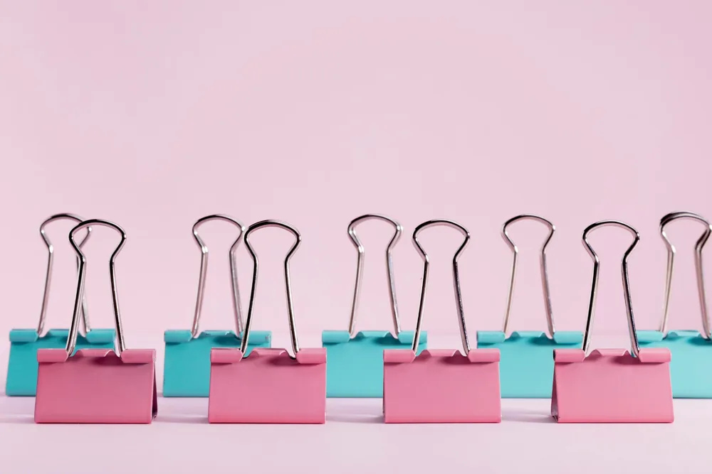 Pinzas para papel rosas y turquesas alineadas en filas sobre un fondo rosa